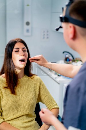 Photo for The ENT doctor examines the patient in the office of the clinic, checks the oral and nasal cavity ear canals with professional instruments - Royalty Free Image