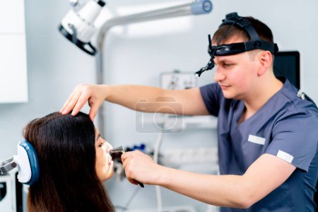 Téléchargez les photos : Le médecin ORL examine le patient au cabinet de la clinique, vérifie les canaux auditifs de la cavité buccale et nasale avec des instruments professionnels - en image libre de droit
