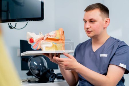 Photo for An ENT doctor consults a patient in the clinic's office tells about the possible consequences of the operation shows ear and nasal canals - Royalty Free Image