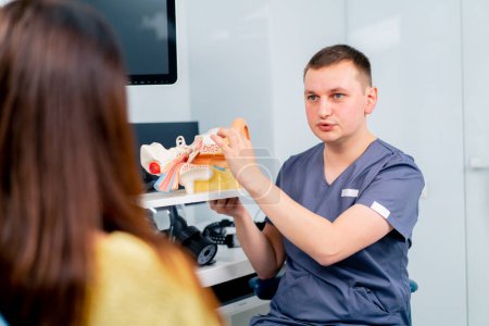 Foto de Un médico de ORL consulta a un paciente en el consultorio de la clínica le informa sobre las posibles consecuencias de la operación muestra el oído y los canales nasales - Imagen libre de derechos