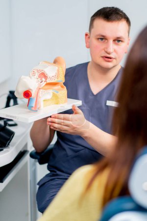 Foto de Un médico de ORL consulta a un paciente en el consultorio de la clínica le informa sobre las posibles consecuencias de la operación muestra el oído y los canales nasales - Imagen libre de derechos