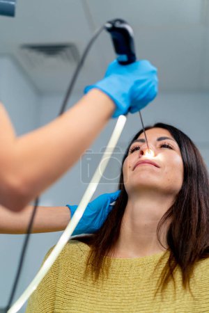 Téléchargez les photos : Gros plan le médecin ORL effectue la procédure d'endoscopie du nez du patient dans la clinique en tenant un dispositif professionnel dans sa main - en image libre de droit