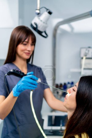 Téléchargez les photos : Le médecin ORL effectue la procédure d'endoscopie du nez du patient dans la clinique en tenant un dispositif professionnel à la main - en image libre de droit