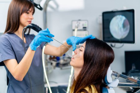 Téléchargez les photos : Le médecin ORL effectue la procédure d'endoscopie du nez du patient dans la clinique en tenant un dispositif professionnel à la main - en image libre de droit