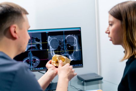 Foto de El médico radiólogo observa la pantalla en la que la imagen 3D de la exploración de la nariz muestra al paciente lo que necesita cambiar durante la cirugía - Imagen libre de derechos