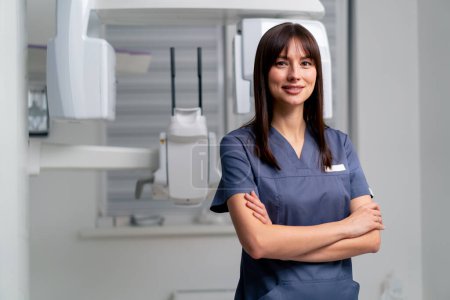 Téléchargez les photos : Portrait d'une belle jeune femme médecin dentiste ou radiologue en uniforme debout avec les bras croisés dans une clinique de beauté et de santé - en image libre de droit
