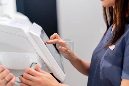 Téléchargez les photos : Une femme médecin effectue une numérisation 3D du nez et de la cavité buccale du patient et clique sur l'écran de l'appareil dans une clinique de chirurgie plastique - en image libre de droit