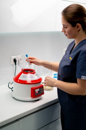 Foto de Médico cosmetólogo enfermedad infecciosa pone tubos de ensayo al dispositivo para llenarlos o laboratorio limpio u hospital - Imagen libre de derechos