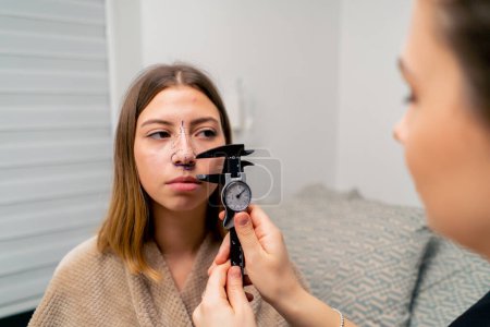 Téléchargez les photos : Médecin en gros plan détient un instrument ORL pour mesurer le nez d'une patiente avant la chirurgie plastique en clinique - en image libre de droit