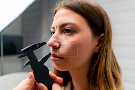 Foto de Primer plano médico sostiene un instrumento de otorrinolaringología para medir la nariz de una paciente antes de la cirugía plástica en la clínica - Imagen libre de derechos