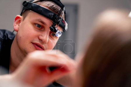 Photo for Portrait of an ENT doctor with a professional headlamp examining a patient in clinic's office - Royalty Free Image