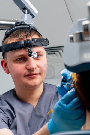 Foto de Retrato de un médico otorrinolaringólogo con un faro profesional examinando a un paciente en el consultorio de la clínica - Imagen libre de derechos