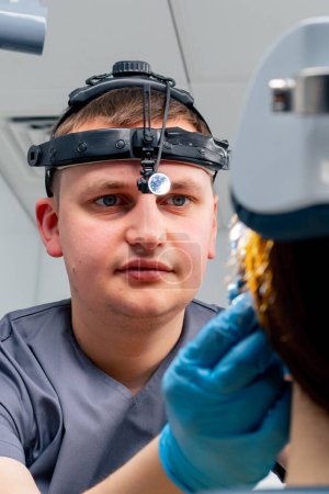 Foto de Retrato de un médico otorrinolaringólogo con un faro profesional examinando a un paciente en el consultorio de la clínica - Imagen libre de derechos
