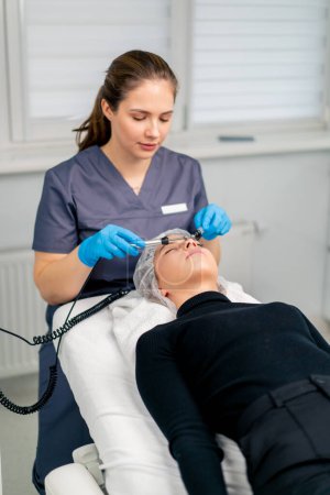 Téléchargez les photos : Un esthéticien massant la peau du visage d'un client pendant la procédure cosmétique de beauté et de santé - en image libre de droit