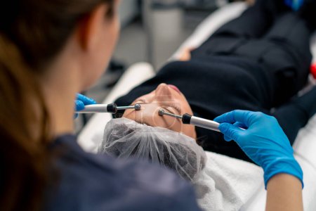 Foto de Un médico esteticista masajeando la piel de la cara de un cliente durante el procedimiento cosmético de belleza y salud - Imagen libre de derechos