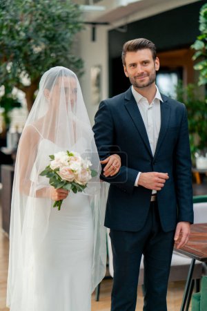 Téléchargez les photos : Portrait d'amoureux souriants le marié conduit la mariée dans une robe blanche et voile à l'autel jeunes mariés au mariage - en image libre de droit