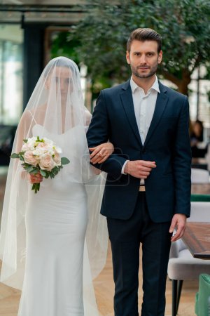 Foto de Retrato de los amantes sonrientes el novio lleva a la novia en un vestido blanco y velo al altar recién casados en la boda - Imagen libre de derechos
