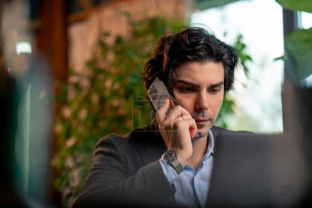 Téléchargez les photos : Portrait d'un homme sérieux un homme d'affaires travaille sur un ordinateur portable dans le bureau communique avec ses collègues sur smartphone - en image libre de droit