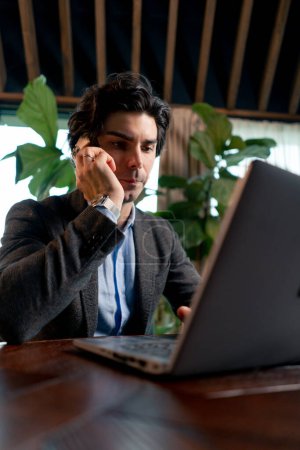 Foto de Retrato de un hombre serio un hombre de negocios trabaja en una computadora portátil en la oficina se comunica con sus colegas en el teléfono inteligente - Imagen libre de derechos