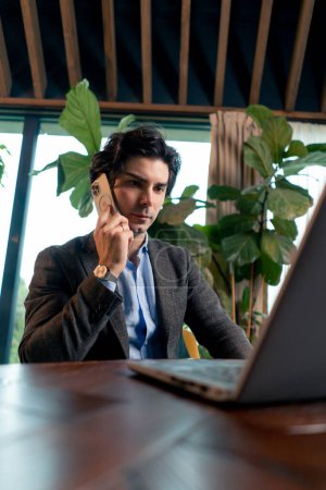 Photo for Portrait of a serious man a businessman works at a laptop in the office communicates with colleagues on smartphone - Royalty Free Image