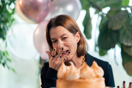 Photo for Portrait of a happy birthday girl who eats a festive cake with pleasure and licks her fingers during a party in restaurant with gifts - Royalty Free Image