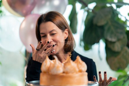 Photo for Portrait of a happy birthday girl who eats a festive cake with pleasure and licks her fingers during a party in restaurant with gifts - Royalty Free Image