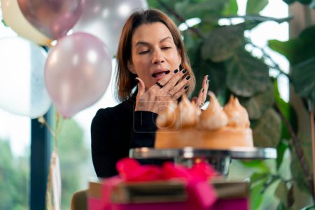 Téléchargez les photos : Portrait d'une fille d'anniversaire heureuse qui mange un gâteau festif avec plaisir et se lèche les doigts lors d'une fête au restaurant avec des cadeaux - en image libre de droit