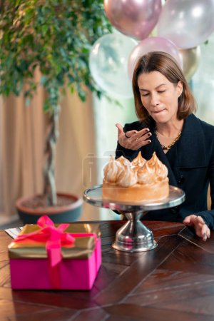 Foto de Retrato de una chica feliz cumpleaños que come un pastel festivo con placer y se lame los dedos durante una fiesta en el restaurante con regalos - Imagen libre de derechos