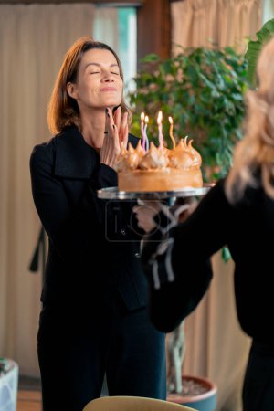 Photo for Portrait of happy birthday girl looking at birthday cake and making wish blowing out candles during party in restaurant - Royalty Free Image