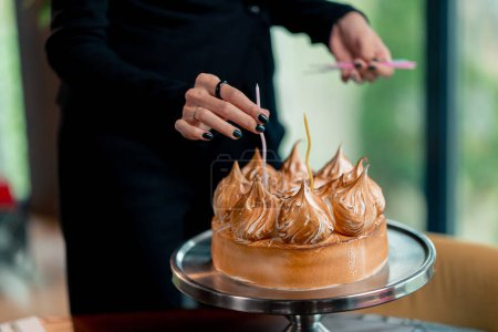 Téléchargez les photos : Gros plan d'une main mettant des bougies dans un délicieux gâteau appétissant lors d'une fête d'anniversaire au restaurant - en image libre de droit