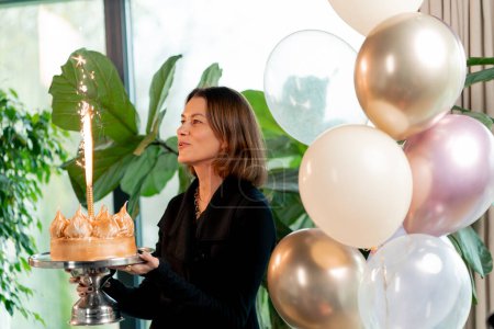 Photo for Portrait of a happy birthday woman holding a festive cake with a candle and making a wish during party in a restaurant - Royalty Free Image