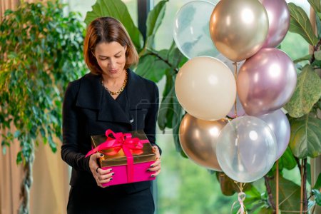 Photo for Portrait of a happy female birthday girl holding a bright gift box during a birthday celebration in restaurant - Royalty Free Image