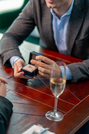 Téléchargez les photos : Un gros plan d'une date dans un restaurant qu'un homme demande en mariage à sa bien-aimée tient une boîte avec une bague - en image libre de droit