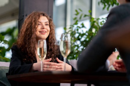 Téléchargez les photos : Portrait d'une jeune femme bouclée lors d'une réunion d'affaires avec un collègue ou lors d'un rendez-vous avec un homme à lunettes champagne célébration - en image libre de droit