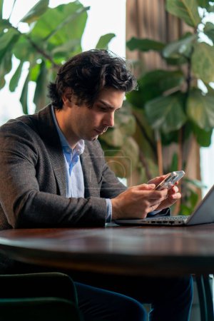 Foto de Retrato de un hombre de negocios serio que trabaja en una computadora portátil en la oficina comprobando la caída del mercado de valores con teléfono inteligente - Imagen libre de derechos