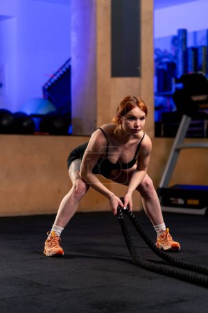 Photo for In a sports club a red-haired trainer bends over and does an exercise with ropes - Royalty Free Image