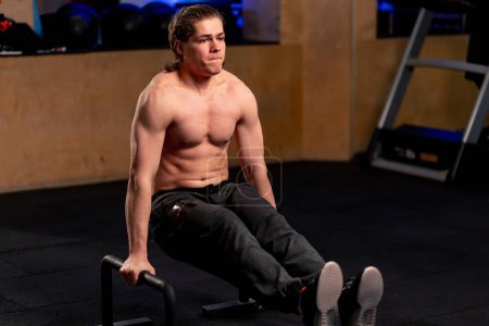 Photo for In a sports club a guy trainer in black sweatpants is doing an exercise on the floor horizontal bar - Royalty Free Image