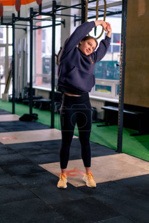 Téléchargez les photos : Dans la salle de gym une coach girl dans un pantalon de survêtement chaud debout faire un échauffement avant l'entraînement - en image libre de droit