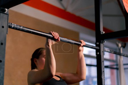 Photo for In the gym coach girl in black leggings and a top is doing pull-ups on the horizontal bar - Royalty Free Image