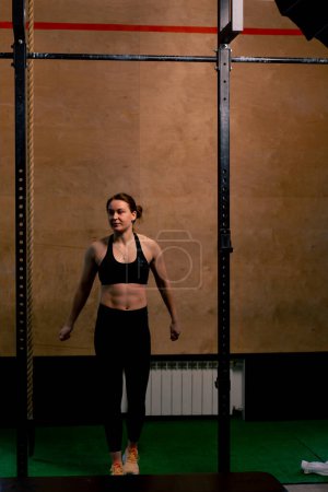 Foto de En el gimnasio una chica entrenador en leggings negro y una parte superior se encuentra cerca de la barra horizontal - Imagen libre de derechos