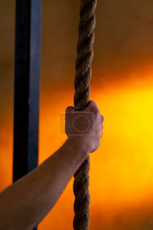 Foto de Primer plano en un club deportivo de una mano sosteniendo cuerdas para hacer ejercicio sobre un fondo naranja brillante - Imagen libre de derechos