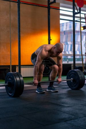 Photo for In a sports club bald trainer in sports shorts lifts weights on a barbell - Royalty Free Image
