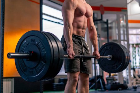 Photo for Close up in a sports club bald trainer in sports shorts lifts weights on a barbell - Royalty Free Image