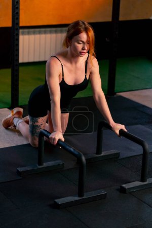 Photo for In a sports club on an orange background a red-haired coach does push-ups on a floor horizontal bar - Royalty Free Image