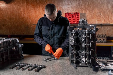 Photo for At a service station on the table a young engine repairman assembles a new piston part - Royalty Free Image