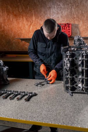 Téléchargez les photos : Dans une station-service sur la table, un jeune réparateur de moteurs assemble une nouvelle pièce de piston - en image libre de droit