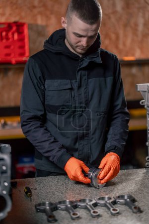 Photo for At a service station on the table a young engine repairman assembles a new piston part - Royalty Free Image