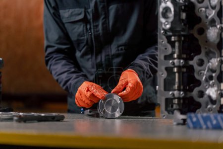 Photo for Close-up At a service station on the table a young engine repairman assembles a new piston part - Royalty Free Image