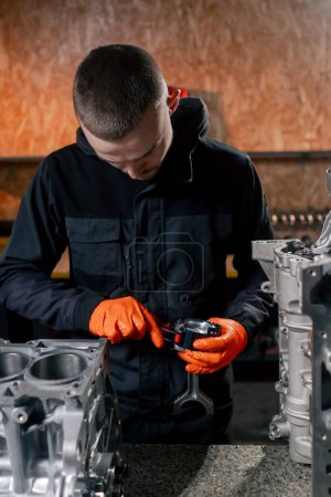 Photo for At a service station on the table a young engine repairman puts a piston part in place - Royalty Free Image