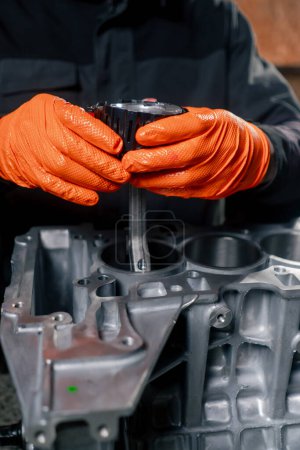 Photo for Close-up At a service station on the table a young engine repairman puts a piston part in place - Royalty Free Image